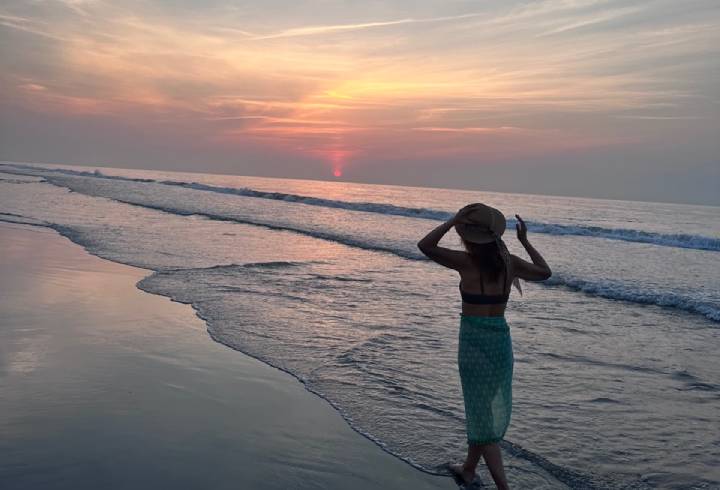 Woman on beach during sunset, wearing hat.