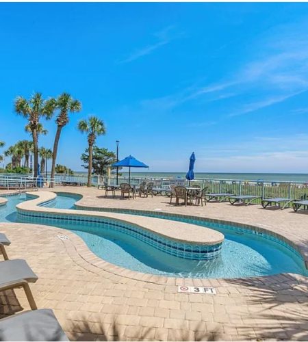 Poolside view with ocean and palm trees.